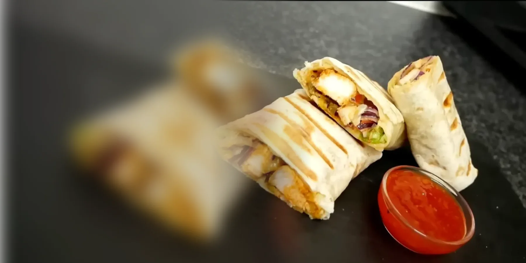 Cookout crispy chicken wrap cut in half with lettuce and a cup of dipping sauce